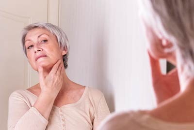 Mulher acima dos 50 anos observando seu pescoço envelhecido com rugas